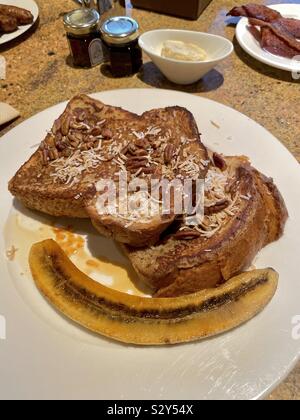 Toast alla francese colazione con noci pecan e topping di noce di cocco con pancetta, condimenti e un acero sauté di banana Foto Stock