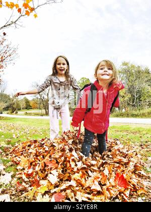 Due giovani ragazze giocando in foglie di autunno Foto Stock