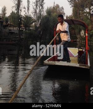 Un uomo utilizza un palo a guidare la sua trajinera attraverso i canali di Xochimilco, Messico. Foto Stock