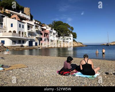 Lucertole da mare e nuotatori a Sa Tuna spiaggia vicino a Begur in Costa Brava, Spagna su un soleggiato e caldo giorno di novembre. Foto Stock