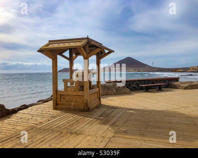 Strandpromenade in El Médano auf Teneriffa mit Blick auf den Rettungsturm, das Meer und die Berglandschaft im Hintergrund Foto Stock