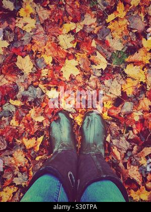 Punto di vista immagine in prospettiva di persona che guarda wet stivali di gomma in wet Foglie di autunno Foto Stock