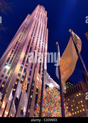 L'iconico albero di Natale brilla luminoso alla base del grattacielo roccia 30 ed è circondato da argento e oro bandiere durante la stagione delle vacanze, NYC, STATI UNITI D'AMERICA Foto Stock