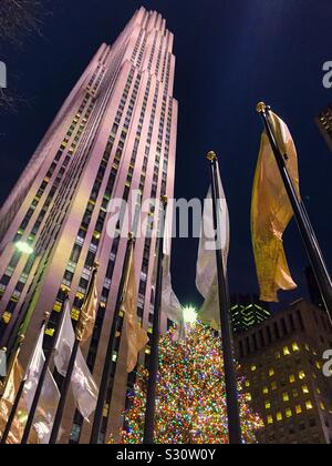 L'iconico enorme albero di Natale al Rockefeller Center brilla luminoso tra argento e oro bandiere alla base della roccia 30, NYC, STATI UNITI D'AMERICA Foto Stock