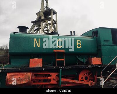 La locomotiva motore utilizzato per il trasporto di carbone dal Maria Colliery, Lochore Prati, Fife, con il cemento armato di avvolgimento testa ingranaggi telaio dell'albero del pozzo 2 in background Foto Stock