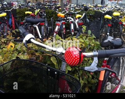 Closeup colpo di un rosso e bianco macchiato il campanello per biciclette e moto parcheggiata in background. Uppsala city stazione ferroviaria parcheggio presto per ospitare un enorme all'interno parcheggio nuovo sito. Svezia Foto Stock