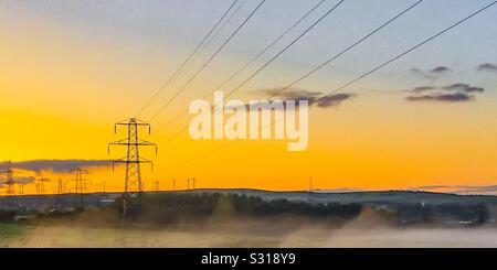 Sunrise su linee di alimentazione nella nebbia di mattina Foto Stock