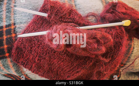 Maglia in lana mohair, aghi da maglia e palline di lana su un plaid coperta. Foto Stock