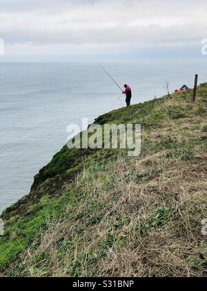 Pescatore sulla sommità di un 300 ft cliff Foto Stock