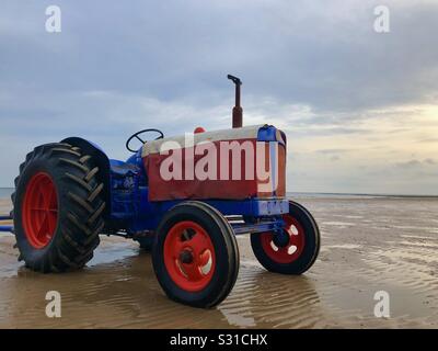 Un luminoso blu e il trattore rosso attende su Redcar beach per la restituzione di barche da pesca Foto Stock