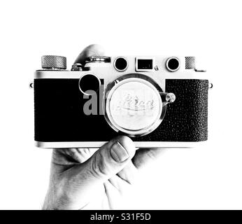 Una fotografia in bianco e nero ad alto contrasto di una mano dell'uomo che tiene una Leica IIf con una lente da 35 mm f/3.5 Elmar Foto Stock