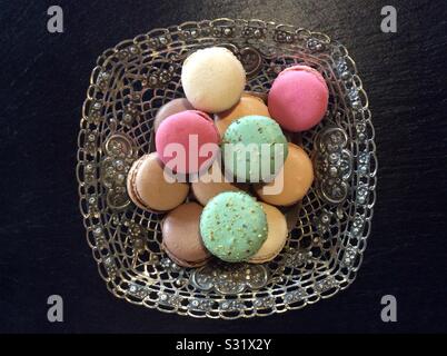 Deliziosi i tradizionali colorati macarons in una pasticceria di argento ciotola su sfondo nero - una piccola torta circolare costituito da due semigusci che racchiudono un ripieno cremoso. Foto Stock