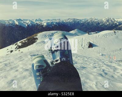 Gambe negli scarponi da sci che si trovano sulla neve in cima al comprensorio sciistico di Zoncolan, Italia. Dolomiti sullo sfondo. Foto Stock