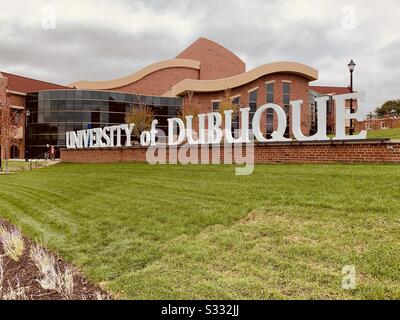 Dubuque, IOWA, 10/19--Paesaggio foto di lettere bianche segnaletica montata su un muro di mattoni sulla riva erbosa di erba verde di fronte al bellissimo edificio rosso mattone arti dello spettacolo sul campus UD. Foto Stock