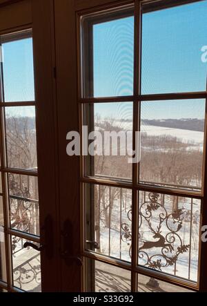 Dubuque, IOWA, 23/02/2020 – Foto di una porta di legno dal design intricato e finestre panoramiche con splendida vista panoramica sui terreni agricoli innevati nelle giornate di sole. Foto Stock