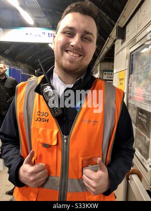 Uomo London Underground lavoratore sorridente indossare giubbotto di sicurezza assistere pendolari Foto Stock