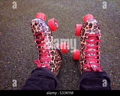 Primo piano di un paio di pattini a rotelle con stampa leopardata indossati da una donna seduta sul tarmac, riposante o pronta per andare a pattinare Foto Stock