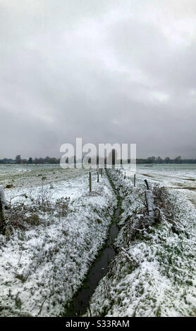 Due campi agricoli divisi da un torrente e sotto una coperta di neve con un cielo grigio nuvoloso neve riempito sopra Foto Stock