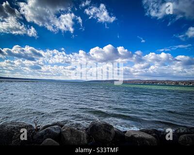 Vista panoramica del lago d'acqua dolce di New York da una spiaggia rocciosa con nuvole di cumuli in un cielo blu Foto Stock