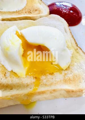 Perfetto uovo in camicia runny su toast con salsa di pomodoro sullo sfondo Foto Stock