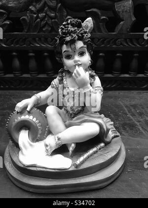 Bambino Krishna mangiare burro- cute piccola statua di cera trovato in un negozio di artigianato in Little India Arcade, Singapore-Hindu Dio Sri Krishna-Janmashtami-Lord shri Krishnan - Soulful Amore di Dio-nero & bianco Foto Stock