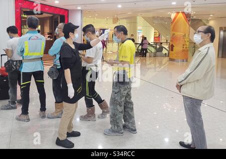Hongkongers indossando maschere e la loro febbre che è stato controllato durante l'attesa in linea in un ristorante durante la pandemia di Covid-19. Foto Stock