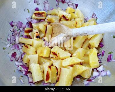 Preparazione di un piatto di ananas in cucina. Preparazione di frutta fresca e matura. Ingredienti per la salsa di ananas fatta in casa. Pezzi alla griglia con cipolla rossa, succo di lime e coriandolo in una terrina di acciaio. Foto Stock