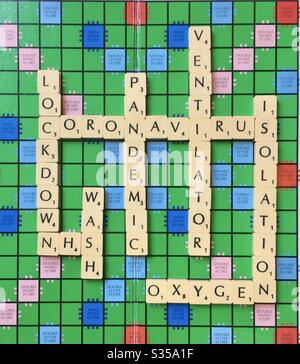 Parole relative alla pandemia del coronavirus, disposte in piastrelle Scrabble su un tabellone di gioco Scrabble Foto Stock