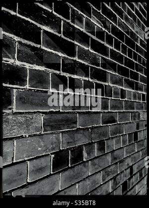 Foto in bianco e nero di un muro di mattoni scuri con prospettiva angolata Foto Stock