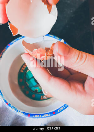 Un bambino che rompe le uova in una ciotola di plastica. Foto Stock