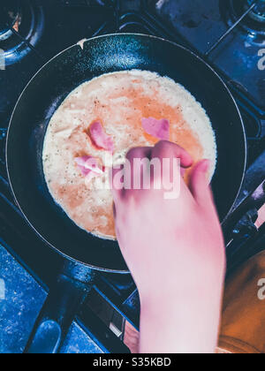 La mano di un bambino spruzza il prosciutto in un'omelette. Foto Stock