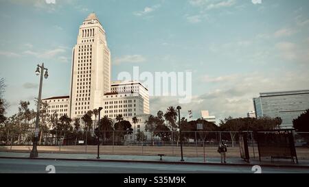 LOS ANGELES, CA, Apr 2020: L'uomo attende l'autobus con il Municipio sullo sfondo del quartiere del Centro Civico nel centro città. Foto Stock