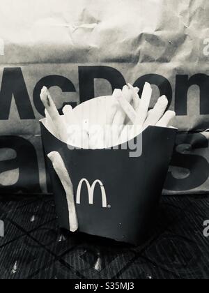 Una porzione delle patatine fritte di McDonald su un sacchetto di carta MCD di sfondo - una singola patatine si attaccano fuori dalla scatola, rapidamente ha preso un schiocco. Yummy junk food mai, fast food veloce snack in qualsiasi momento, b & w Foto Stock