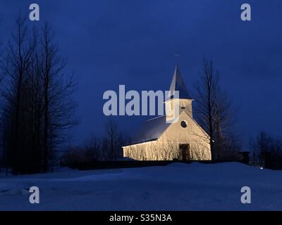 Una piccola e semplice chiesa in Islanda nel mezzo del nulla, illuminata contro il cielo scuro. Ora blu. Foto Stock