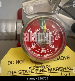 Dettaglio del manometro rosso su un estintore chimico a secco con etichetta di ispezione gialla del maresciallo antincendio Foto Stock