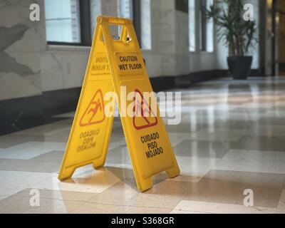 LOS ANGELES, CA, Apr 2020: Primo piano sull'insegna gialla "attenzione, pavimento bagnato" nella lobby piastrellata in marmo con luce naturale proveniente dalle finestre laterali. Foto Stock