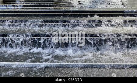 Dettaglio di spruzzi d'acqua e di scale di marmo scuro che cadono nella luce del giorno Foto Stock