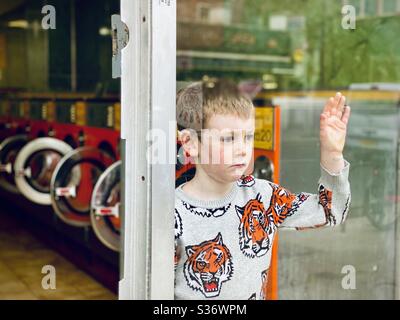 Un ragazzo bianco si stigra da una finestra di lavanderia Foto Stock