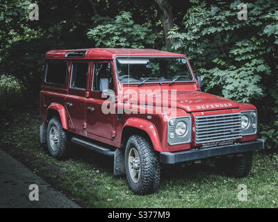 Red Land Rover Defender 110, vettura a trazione integrale parcheggiata su erba Foto Stock
