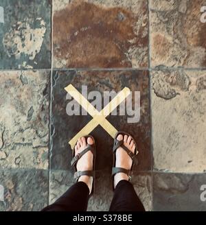 Ragazza in piedi su pavimenti in piastrelle segnate con la x gialla durante il coronavirus pandemic sociale distancing USA, America Foto Stock
