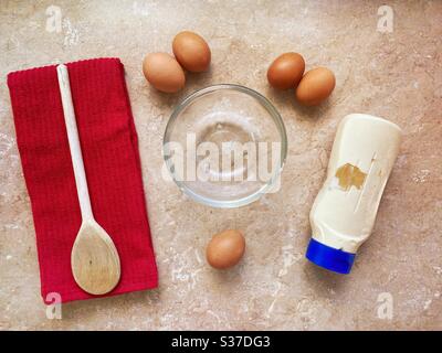 Preparazione di ingredienti per la maionese all'uovo fatta in casa in cucina. Visto dall'alto. Vista dall'alto verso il basso. Piatto posare preparazione alimentare con utensili, uova, bottiglia di salsa mayo e cucchiaio di legno sul banco. Foto Stock