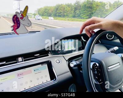 Mani di un uomo sul volante di una Range Rover Evoque. Dettagli del cruscotto interno moderno. Guida in autostrada con navigatore satellitare. Libertà, avventura, viaggio su strada. Con deodorante per ambienti unicorno Foto Stock