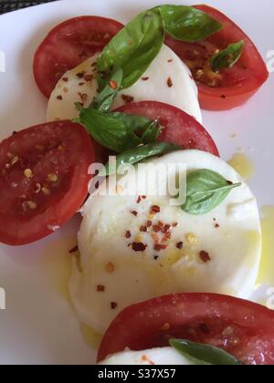 Ancora vita di un'insalata di fette di mozzarella, basilico fresco, pomodori maturi di vite ricoperti di un composto di olio d'oliva piccante Foto Stock