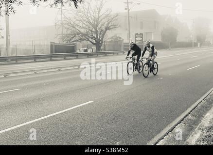 Due ciclisti percorrono la Pacific Highway a Gordon A Sydney in una mattinata invernale molto scialba Foto Stock