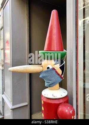 Personaggio di Pinocchio che indossa la maschera COVID-19 al di fuori del negozio di giocattoli Jeu Jouet, Rue de l’Aiguillerie, Angers, Maine-et-Loire, Francia. Foto Stock
