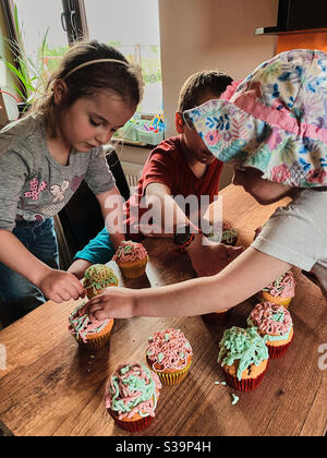 Gruppo di bambini che cuocce, prepara ingredienti, condimenti, spolverate per decorare i biscotti. I bambini imparano a cucinare, lavorando insieme in cucina a casa. Concetto di famiglia felice Foto Stock