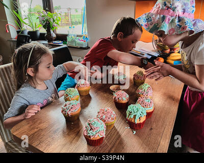 Gruppo di bambini che cuocce, prepara ingredienti, condimenti, spolverate per decorare i biscotti. I bambini imparano a cucinare, lavorando insieme in cucina a casa. Concetto di famiglia felice Foto Stock