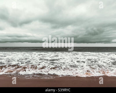 Stagcape con copertura nuvolosa bassa. Onde oceaniche che si lavano sulla spiaggia di sabbia durante il giorno e overcast. Foto Stock