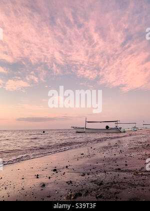 Jukung barca sulla spiaggia con il cielo rosa che si riflette sulla sabbia durante il tramonto a Lovina, Bali Foto Stock