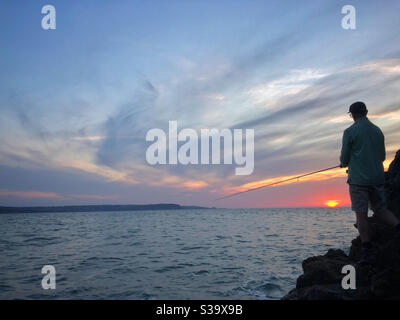 Pesca di pescatori al tramonto sulla costa gallese, settembre. Foto Stock